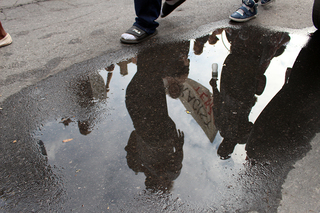 Reflections of the marching crowd show in the puddles on the road from earlier rain.