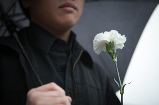 Daniel Nguyen, a Junior Syracuse University student, holds a white flower in front of the Wall of Remembrance.